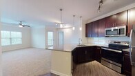 This single-floor residence offers a thoughtfully designed open-concept layout where the kitchen flows seamlessly into the living area. The kitchen is a standout feature, outfitted with rich dark-espresso cabinetry, granite countertops, a subway tile backsplash, and a full suite of stainless steel appliances including a refrigerator, electric range, and built-in microwave. A peninsula with an integrated sink and pendant lighting above serves as both a functional workspace and a natural divider between the kitchen and living space. Track lighting and crown molding add refined detail throughout the common areas.

The living room is generously proportioned, finished with plush neutral carpeting and access to an outdoor balcony, allowing natural light to filter through. The bedrooms are comfortably sized, each featuring ceiling fans, large windows with outdoor views, and soft carpeting underfoot.

Two bathrooms mirror the kitchen's design aesthetic, featuring dark cabinetry—one in espresso, one in navy blue—granite-topped vanities, large mirrors, wood-look flooring, and soaking tub and shower combinations. The overall ambiance is clean, modern, and cohesive throughout.