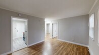 This 2-bedroom, 1-bathroom single-floor unit offers a clean, modern aesthetic with a cohesive design throughout. Warm-toned hardwood-style flooring runs through the main living areas and bedrooms, complemented by neutral gray walls and crisp white trim that create a bright, fresh atmosphere.

The living room is a welcoming, open space featuring multiple windows that invite natural light and baseboard heating for year-round comfort. A white paneled entry door provides direct access to the unit. The kitchen is thoughtfully equipped with white cabinetry, granite-style countertops, a stainless steel sink with a matte black faucet, and stainless steel appliances, including a refrigerator and electric range. Light hardwood-style flooring and a direct sightline into the living area give the kitchen an open, connected feel.

Both bedrooms are comfortably scaled, each featuring neutral gray walls, hardwood-style flooring, baseboard heating, and windows with blinds. One bedroom includes a window-mounted air conditioning unit for added climate control. A secondary entry door is also accessible from one of the bedrooms.

The bathroom is neatly finished with light tile flooring, wainscoting, a combined tub and shower, a pedestal-style sink, and matte black fixtures and accessories. A window with blinds provides ventilation and natural light. The overall layout is efficient and functional, making excellent use of the available space.