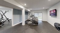 Located in St. Louis Park, MN, this fitness center offers a comprehensive workout environment designed to accommodate a wide range of exercise routines. The space is organized across a single floor and divided into two interconnected areas, each serving a distinct fitness purpose.

The main workout area features durable rubber flooring throughout, providing both safety and sound absorption. A multi-station cable machine anchors the strength training zone, complemented by a well-stocked dumbbell rack and an adjustable weight bench. Motivational wall phrases, including "Trust the Process" and "Challenge Yourself, Change Yourself," set an energizing tone. Fluorescent and recessed lighting ensures the space is well-lit throughout.

The cardio zone houses multiple treadmills and elliptical machines, arranged to maximize floor space. A sliding glass door in this area allows natural light to filter in and offers a view of the outdoor surroundings. Recessed ceiling lights and a wall-mounted television add to the functionality of this section. Step platforms and additional accessories are neatly stored along the walls.

White structural columns and clean white walls give the facility a bright, open feel. The layout is practical and efficient, making it a well-rounded amenity for residents seeking a convenient on-site fitness option.