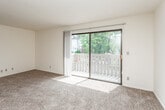 This single-floor unit offers a practical and comfortable layout across several well-defined living spaces. The spacious living room serves as the heart of the home, finished with plush wall-to-wall carpeting and a textured ceiling. A large sliding glass door floods the room with natural light and opens directly onto a private balcony, which overlooks a lush, tree-lined outdoor setting. A ceiling fan adds to the comfort of the space. Adjacent to the living area, the kitchen is outfitted with warm-toned wood cabinetry — both upper and lower — paired with light wood countertops and tile flooring. A coil-burner electric range and a dishwasher are included appliances, and a ventilation hood is installed above the range. The bedroom is generously sized, featuring carpet flooring, a large sliding-door closet offering ample storage, and a window that brings in natural light. The full bathroom includes a single-sink vanity with dark wood cabinetry, a toilet, and a full-length soaking tub with shower, all set on warm tile flooring. Throughout the unit, neutral cream-toned walls and dark wood door accents create a cohesive, understated aesthetic.