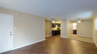 This single-floor unit offers a thoughtfully designed layout with a cohesive, neutral color palette of warm beige tones and crisp white trim throughout. The open living area is generously sized, featuring rich, dark wood-style flooring that extends seamlessly throughout the main spaces, creating a warm and inviting ambiance. A sliding glass door with vertical blinds allows natural light to fill the room, enhancing its open feel.

The kitchen is efficiently laid out and features bold, dark espresso-toned cabinetry with sleek hardware, light granite-style countertops, a stainless steel sink, and black appliances including a range and dishwasher. An overhead range hood and under-cabinet lighting add to the kitchen's functional design. The kitchen flows naturally from the living area, making the space ideal for everyday living.

The bathroom includes a dark vanity cabinet paired with granite-style countertops and a wide mirror, offering ample prep space. A separate water closet with wood-style flooring provides added privacy. The walk-in closet is notably spacious, featuring dual hanging rods on multiple walls and plush carpeting underfoot, offering generous storage capacity. Ceiling fans with integrated lighting are present in key areas, contributing to the unit's practical and comfortable design.