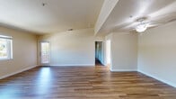 Located at 6175 Water Lily Common in Livermore, CA, this single-story home offers a clean, functional layout designed for comfortable everyday living. The main living area is a standout feature, boasting dramatic vaulted ceilings that create an airy, open atmosphere. Warm hardwood-style flooring flows throughout the space, complemented by neutral beige walls and crisp white trim. Natural light filters in through windows and a glass-paneled door, brightening the generous open floor plan. A ceiling fan adds practical comfort to the living area. The kitchen is efficiently designed with white cabinetry, granite-patterned countertops, and white appliances including a range and full-size refrigerator, all set over matching hardwood-style flooring. The bedroom offers a comfortable, well-proportioned space with its own ceiling fan and direct access to the bathroom. The bathroom is neatly finished with a white vanity topped with granite countertops, a large mirror, a tub-shower combination enclosed by sliding glass doors, and hardwood-style flooring. Throughout the home, a consistent design palette of neutral tones, white fixtures, and warm flooring creates a cohesive and inviting ambiance suitable for a variety of lifestyles.
