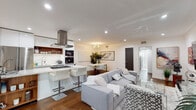 Located at 1267 N Laurel Ave in the heart of West Hollywood, this single-floor residence offers a thoughtfully designed open-concept layout that seamlessly connects the living, dining, and kitchen areas. Rich hardwood flooring runs throughout, anchoring the bright, white interiors and creating a warm contrast against the clean, contemporary finishes.

The kitchen is a standout feature, boasting a dramatic marble-veined waterfall island with a built-in gas cooktop and bar seating, complemented by sleek white cabinetry, a stainless steel range hood, and a full suite of built-in appliances including a wall oven and microwave. A dining area sits adjacent, ideal for entertaining.

The living area is generously proportioned, featuring a wall-mounted flat-screen TV, chrome-accented glass furniture, and curated décor that lends an upscale, editorial feel. A welcoming entryway with a round wood-framed mirror and lush tropical plant sets the tone upon arrival.

The bedroom is a serene retreat with recessed lighting, natural light from a large window, floor-to-ceiling mirrored closet doors, and warm hardwood floors. The bathroom is finished in stunning floor-to-ceiling marble-look tile, featuring a frameless glass walk-in shower with a rain showerhead, offering a spa-like experience.