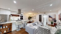 Located at 1267 N Laurel Ave in the heart of West Hollywood, this single-floor residence offers a thoughtfully designed open-concept layout that seamlessly connects the living, dining, and kitchen areas. Rich hardwood flooring runs throughout, anchoring the bright, white interiors and creating a warm contrast against the clean, contemporary finishes.

The kitchen is a standout feature, boasting a dramatic marble-veined waterfall island with a built-in gas cooktop and bar seating, complemented by sleek white cabinetry, a stainless steel range hood, and a full suite of built-in appliances including a wall oven and microwave. A dining area sits adjacent, ideal for entertaining.

The living area is generously proportioned, featuring a wall-mounted flat-screen TV, chrome-accented glass furniture, and curated décor that lends an upscale, editorial feel. A welcoming entryway with a round wood-framed mirror and lush tropical plant sets the tone upon arrival.

The bedroom is a serene retreat with recessed lighting, natural light from a large window, floor-to-ceiling mirrored closet doors, and warm hardwood floors. The bathroom is finished in stunning floor-to-ceiling marble-look tile, featuring a frameless glass walk-in shower with a rain showerhead, offering a spa-like experience.