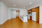Located at 2477 S Moody Ave in Portland, Oregon, this single-floor, three-bedroom, two-bathroom home offers a well-designed layout with a clean, modern aesthetic throughout. The open-concept kitchen and living area serves as the heart of the home, featuring warm-toned hardwood flooring, recessed lighting, and a central kitchen island with a light stone countertop and undermount sink. The kitchen is equipped with medium-toned wood cabinetry extending to the ceiling for ample storage, a white electric range, and a full-size refrigerator. The adjoining living area is bright and open, creating a versatile shared space. A hallway connects the main living areas to the three bedrooms, each finished with plush neutral carpet and ceiling fans. The bedrooms are well-lit by large windows dressed with vertical blinds that allow natural light to filter through. Closets with built-in shelving and hanging rods provide practical storage. The two bathrooms are finished with neutral tile flooring, wood-toned vanity cabinets, stone-top counters, and large mirrors. The overall interior palette of whites, warm woods, and soft neutrals gives the home a cohesive, comfortable, and functional character throughout.
