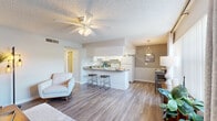 Located at 1211 Goldfinch Dr in Plant City, FL, this 2-bedroom, 1-bathroom single-floor home offers a well-designed layout with a warm, functional aesthetic throughout. The open-concept living, dining, and kitchen area serves as the heart of the home, featuring wood-look flooring, a textured ceiling, and ceiling fans that promote comfortable airflow. The kitchen is outfitted with white cabinetry, a dark-toned countertop peninsula with bar seating, white appliances, and a pendant light above the adjacent dining area, creating a seamless space for cooking and entertaining. The living room provides a bright, welcoming atmosphere with neutral walls and ample room for relaxed seating. The primary bedroom is a comfortable retreat, highlighted by large sliding glass doors that invite natural light and offer views of the outdoors, complemented by a ceiling fan and wood-look flooring. The second bedroom is similarly bright, featuring a wide window with vertical blinds and a ceiling fan, making it well-suited as a guest room or home office. The bathroom includes a full tub-shower combination with clean white tile. Five closets distributed throughout the home ensure generous storage. A hallway connects the private spaces efficiently, completing this practical and inviting floor plan.