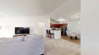 Located at 1 Ascot Cir in Saratoga Springs, NY, this two-bedroom, two-bathroom home spans two floors and offers a thoughtfully designed layout suited for comfortable everyday living. The ground level includes an attached garage with an automatic opener and direct interior access. The main living floor hosts the majority of the home's space, beginning with an open-concept area that seamlessly connects the living room, dining room, and kitchen. The living room is bright and airy, featuring large windows that invite natural light and views of the surrounding greenery, with soft carpeting underfoot. The adjacent dining area features warm hardwood-style flooring, vaulted ceilings, and a pendant light fixture. The kitchen is well-equipped with rich cherry cabinetry, granite countertops, stainless steel appliances, and matching hardwood-style flooring. Both bedrooms are carpeted and generously sized, with the primary bedroom boasting soaring ceilings and tall windows framing lush outdoor views. The two bathrooms feature neutral stone-look vinyl flooring and clean, functional finishes. A dedicated laundry room with a full-size washer adds to the home's practicality. Multiple hallways connect the spaces efficiently throughout the floor plan.