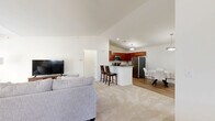 Located at 1 Ascot Cir in Saratoga Springs, NY, this two-bedroom, two-bathroom home spans two floors and offers a thoughtfully designed layout suited for comfortable everyday living. The ground level includes an attached garage with an automatic opener and direct interior access. The main living floor hosts the majority of the home's space, beginning with an open-concept area that seamlessly connects the living room, dining room, and kitchen. The living room is bright and airy, featuring large windows that invite natural light and views of the surrounding greenery, with soft carpeting underfoot. The adjacent dining area features warm hardwood-style flooring, vaulted ceilings, and a pendant light fixture. The kitchen is well-equipped with rich cherry cabinetry, granite countertops, stainless steel appliances, and matching hardwood-style flooring. Both bedrooms are carpeted and generously sized, with the primary bedroom boasting soaring ceilings and tall windows framing lush outdoor views. The two bathrooms feature neutral stone-look vinyl flooring and clean, functional finishes. A dedicated laundry room with a full-size washer adds to the home's practicality. Multiple hallways connect the spaces efficiently throughout the floor plan.