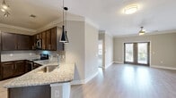 This two-story home offers a thoughtfully designed layout spread across two levels. The main floor opens into a combined kitchen and living area, where light hardwood-style flooring, crown molding, and neutral tones create a clean, contemporary feel. The kitchen is a standout, featuring dark espresso cabinetry, granite countertops, a subway tile backsplash, stainless steel appliances, and a peninsula with a sink and pendant lighting above. The living area is bright and airy, with a ceiling fan, crown molding, and French doors that invite natural light and offer views to the outdoors. A dedicated laundry area and access to the attached garage—equipped with an automatic opener and overhead storage—complete the lower level. Upstairs, the spacious primary bedroom is finished with plush carpet, crown molding, a ceiling fan, and multiple doors leading to closet space and additional rooms. The full bathroom is elegantly appointed with a granite vanity, dark wood cabinetry, subway tile tub surround, and chrome fixtures. A staircase connects the two levels, enhancing the home's functional, multi-level flow throughout.