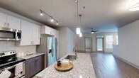 Located at 2440 Bristol Creek Dr in Morrisville, NC, this well-appointed 2-bedroom, 3-bathroom residence offers a thoughtfully designed single-level layout with contemporary finishes throughout. The open-concept kitchen and living area serves as the heart of the home, featuring wood-look flooring, a ceiling fan, and sliding glass doors that invite natural light and provide access to an outdoor balcony with views of the community's resort-style pool and landscaped courtyard. The kitchen is a standout, boasting a large center island with a granite countertop, dark wood cabinetry contrasted by crisp white upper cabinets, a subway tile backsplash, and stainless steel appliances including a French door refrigerator and electric range. Each bedroom is finished with plush carpeting and a ceiling fan. The generously sized primary bedroom connects to a spa-inspired en-suite bathroom featuring a dual granite vanity with modern fixtures and a glass-enclosed walk-in shower clad in large-format marble-style tile. A spacious walk-in closet with wire shelving provides ample storage. The second bedroom similarly offers easy access to its own bathroom. Two dedicated closets add further convenience, rounding out a functional and stylish living space.