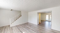 Located at 3419 Westmont St in Mount Vernon, Illinois, this two-story home offers four bedrooms and two bathrooms spread evenly across both floors. The main level welcomes you with an open living area featuring light-toned hardwood-style flooring, crisp white walls, and a distinctive textured ceiling that adds character throughout. A white-railed staircase serves as a central architectural element, connecting both floors with clean lines and a classic design. The living area benefits from natural light streaming through a window with outdoor views of the surrounding greenery. Sliding glass doors provide additional access to the exterior, enhancing the connection between indoor and outdoor spaces. The kitchen and a utility room round out the functional areas on this floor. Upstairs, the four bedrooms are finished with plush carpeting and feature built-in closets with bifold doors, offering practical storage. The spacious primary bedroom provides generous room for furnishings. Both bathrooms are finished with hardwood-style flooring; one includes a full tub-shower combo with tiled surround, a vanity with white countertop, and a wall mirror, while the second offers a more utilitarian layout with a wood-toned shelf and ventilation. The home maintains a consistent, neutral aesthetic throughout, creating a clean and move-in ready environment.