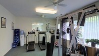 This fitness room is designed to support a well-rounded exercise routine within a compact, efficiently organized layout. The space is furnished with multiple treadmills, an elliptical trainer, and a multi-station cable weight machine, providing options for both cardiovascular and strength training workouts. The flooring consists of durable, low-pile carpet suited for gym use, offering cushioning underfoot during exercise.

Two ceiling fans are installed overhead, promoting consistent air circulation throughout the room to keep the environment comfortable during workouts. Overhead fluorescent lighting supplements the natural light that filters in through windows along one wall, brightening the interior and providing views of outdoor greenery. A wall-mounted mirror expands the perceived depth of the space while allowing users to monitor their form during exercise.

A water cooler is positioned near the entrance, offering convenient hydration access. The walls are finished in a neutral off-white tone, contributing to a clean, no-frills aesthetic. The overall ambiance is practical and functional, focused entirely on providing residents with a well-maintained space dedicated to fitness and physical wellness.