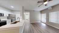 This well-designed single-floor residence offers a clean, contemporary aesthetic throughout, characterized by a neutral gray and white color palette, durable hardwood-style flooring in the main living areas, and crisp white trim and baseboards. The open-concept layout connects the kitchen and living area seamlessly, creating a spacious and functional flow. The kitchen is thoughtfully appointed with white shaker-style cabinetry, light quartz countertops, a stainless steel undermount sink, and a full suite of stainless steel appliances including a refrigerator, electric range, built-in microwave, and dishwasher. A large bi-fold door pantry provides generous storage. The living area benefits from natural light through blinds-fitted windows and a glass door, with a ceiling fan overhead adding both style and comfort. A hallway leads to multiple bedrooms, each featuring plush carpeting, windows with horizontal blinds, and ceiling fans where applicable. The bathroom is outfitted with wood-look tile flooring, a tub-shower combination, a white vanity with quartz countertop, and clean, neutral wall tones. Throughout the unit, the consistent design choices and well-maintained finishes create a bright, move-in-ready atmosphere.