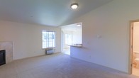 This single-floor unit offers a clean and functional layout designed to maximize comfort and usability. The living area is finished with wall-to-wall carpet and bathed in natural light streaming through large windows, creating a welcoming and airy atmosphere. Flush-mount ceiling lighting provides additional illumination throughout the space. A wall-mounted HVAC unit is conveniently located in the living area, offering climate control year-round. The living space connects seamlessly to the kitchen through a pass-through counter with a built-in sink, enhancing the open feel of the floor plan. The kitchen features tile flooring, overhead lighting, and its own window, allowing for additional natural light and ventilation. The neutral, light-toned walls and ceilings throughout the unit contribute to a bright and versatile interior that can be easily personalized. The open-concept design between the living and kitchen areas promotes a sense of spaciousness, making the unit feel larger than its footprint suggests. Overall, the space presents a practical and comfortable environment suitable for everyday living.