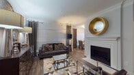 This single-floor residence combines contemporary design with refined finishes throughout its well-organized layout. The living room serves as a central gathering space, featuring a white-mantled fireplace, crown molding, wood-look flooring, and large windows dressed with grommet-panel curtains that allow natural light to filter through. A geometric-patterned area rug and mirrored accent furniture contribute to the room's polished aesthetic.

The dining area accommodates a round table with tufted upholstered chairs, situated beside bright windows that enhance the open feel of the space. The kitchen is outfitted with white cabinetry, granite countertops, a subway tile backsplash, and stainless steel appliances, including a range, microwave, and dishwasher.

The bedrooms are carpeted and thoughtfully designed. One features crown molding, wide windows, and star-burst wall décor, while another offers a more neutral, earthy palette with a low-profile dresser and framed artwork. A third bedroom space includes a decorative credenza with a mirrored accent mirror above.

Two bathrooms serve the residence — one with a soaking tub and tiled surround, the other featuring a white vanity with quartz-style countertop, wood-look flooring, and contemporary wall art.