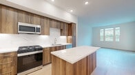 Located at 1205 Aviara Parkway in Carlsbad, CA, this well-appointed 2-bedroom, 2-bathroom single-story residence offers a thoughtfully designed layout with modern finishes throughout. The open-concept kitchen is a standout feature, showcasing rich wood cabinetry, a striking marble-style quartz backsplash, a center island with a waterfall-edge quartz countertop, and a full suite of stainless steel appliances including a gas range, built-in microwave, dishwasher, and French door refrigerator. Light hardwood flooring flows seamlessly through the living areas, complementing the clean white walls and recessed lighting. The spacious living area receives abundant natural light through large windows with views of lush greenery, with access to a private balcony. The generously sized primary bedroom includes a walk-in closet with built-in shelving and rod systems. Both bathrooms are finished with large-format tile flooring, wood-toned vanities, and white quartz countertops; the primary bath features a glass-enclosed walk-in shower with marble-style tile surround. Additional conveniences include dedicated closets, a laundry area, and a connecting hallway that ties the layout together efficiently.