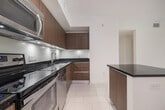 Located at 939 NW 97th Ave, Unit 110 in Miami, FL, this ground-floor residence offers 940 square feet of single-story living across two bedrooms, three bathrooms, and a dedicated laundry room. The open-concept kitchen and living area anchors the unit with large-format white tile flooring, track lighting, and a functional layout. The kitchen is outfitted with warm wood cabinetry, dark granite countertops, stainless steel appliances including a French door refrigerator and gas range, and a peninsula that separates the cooking area from the living space. The bathrooms maintain a consistent modern aesthetic, featuring wood vanities with granite counters and large-format tile. At least one bathroom includes a full soaking tub with subway-style tile surround. Both bedrooms feature neutral carpet flooring, windows with exterior views to a landscaped green area, and access to closets equipped with wire shelving systems. The primary bedroom measures 150 square feet and includes its own closet. A dedicated in-unit laundry room accommodates a full-size washer and dryer. The unit's clean, neutral palette and cohesive finishes create a practical and contemporary living environment.