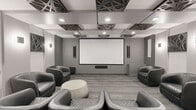 Located at 1792 Pembina Highway in Winnipeg, this purpose-built screening room delivers a refined and immersive home theatre experience within a compact, single-floor layout. The room's centrepiece is a large wall-mounted projection screen paired with a ceiling-mounted projector and a soundbar, providing a dedicated cinematic setup. Seating consists of multiple quilted black leather swivel tub chairs arranged to face the screen, offering comfortable, lounge-style viewing for small groups. The ceiling is a standout architectural feature, adorned with geometric laser-cut decorative panels in a dark finish, complemented by recessed pot lighting that creates a focused, ambient atmosphere. The grey-toned walls are accented with modern wall sconces, slim vertical speakers, and decorative wall art echoing the ceiling's geometric motif. Flooring transitions between textured carpet tiles in the viewing area and smooth hardwood near the kitchenette. The kitchenette area is well-equipped with grey cabinetry, open shelving, a microwave, a stainless steel refrigerator, and a sink — making the space fully self-contained for hosting. A wall-mounted mini-split unit ensures climate control. Overall, the space presents a cohesive, contemporary aesthetic in a neutral grey palette throughout.