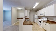 This well-appointed single-floor residence offers three bedrooms and two full bathrooms within a thoughtfully designed layout. The kitchen is a standout feature, showcasing white cabinetry, dark granite-style countertops, a peninsula breakfast bar, and white appliances including a range, microwave, and refrigerator. Light ceramic tile flooring runs throughout the kitchen and main areas, while elegant crown molding adds a refined architectural touch. The kitchen opens toward the living area, creating a connected and functional flow. The bedrooms are finished with plush carpet flooring and neutral-toned walls, providing a calm and comfortable atmosphere. The primary bedroom includes direct access to an en-suite bathroom, offering added convenience and privacy. The secondary bedrooms are generously proportioned, with one featuring a double-door closet and a window that brings in natural light. Both bathrooms are finished with clean white vanities, tile flooring, and tub-shower combinations equipped with grab bars, blending practicality with a clean aesthetic. Throughout the home, the consistent neutral color palette and classic finishes create a cohesive, move-in-ready environment suited for a range of lifestyles.