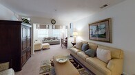 This single-story residence offers a thoughtfully designed layout that balances comfort and functionality across its many rooms. The living area serves as the heart of the home, featuring plush carpeting, multiple seating arrangements, and abundant natural light streaming through windows dressed with decorative valances. A secondary sitting area provides additional space for relaxation, complete with coordinating window treatments and framed wall art.

The galley-style kitchen is lined with warm oak cabinetry extending to the ceiling, offering generous storage capacity. It is equipped with a full suite of appliances, including a range, refrigerator, and dishwasher, alongside continuous countertops and a double basin sink.

The dining area accommodates a dark-toned table with seating for multiple guests, accented by a striking circular metal wall sculpture that serves as a focal point.

The bedrooms are carpeted and well-sized, each featuring closets and windows that allow natural light. The primary bedroom includes a dedicated closet area, while additional bedrooms offer comparable comfort and storage.

Two full bathrooms each include a tub-shower combination. One features tile flooring and warm wood cabinetry, while the other presents a clean, neutral aesthetic with practical fixtures throughout.