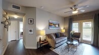 This single-story residence at 7938 City Base Landing in San Antonio, Texas, offers a well-appointed layout finished with consistent dark hardwood-style flooring throughout the main living areas and rich carpet in the bedrooms. The inviting living room features a ceiling fan, neutral-toned walls, and large sliding glass doors that open to a private patio, allowing natural light to fill the space. A decorative media cabinet and colorful abstract artwork add character to the room.

The kitchen is equipped with warm-toned wood cabinetry, granite-style countertops, a mosaic tile backsplash, and black appliances including a refrigerator, range, and dishwasher. A kitchen island with a sink provides added workspace, while an adjacent dining area accommodates casual meals.

The bedrooms offer a serene retreat with plush carpeting, ceiling fans, and windows that bring in natural light. Each room provides comfortable proportions suited for restful living.

The bathrooms are finished with rich wood vanities topped with granite-style counters, large mirrors with lighted fixtures, and tub-shower combinations with tile surrounds and dark hardwood-style flooring, maintaining a cohesive design throughout.

Overall, the residence presents a warm and cohesive aesthetic with thoughtful finishes and a practical, comfortable floor plan.
