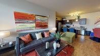This single-story unit offers a thoughtfully designed open-concept layout that connects the living area, dining space, and kitchen into one cohesive environment. The living room features wood-style flooring, a ceiling fan, and large windows that bring in natural light, complemented by bold abstract artwork and a tufted sofa with colorful accent pillows. A dark-finished coffee table and area rug anchor the space with contemporary style.

The kitchen is well-equipped with dark espresso cabinetry, granite countertops, and a full suite of stainless steel appliances including a refrigerator, dishwasher, microwave, and range. A built-in wine rack adds a distinctive touch, while pendant lighting illuminates a granite-topped island with bar seating — ideal for casual dining or entertaining.

The two bedrooms are carpeted and receive natural light through large windows fitted with blinds and curtains. Each room is comfortably sized and includes ceiling fans.

Two full bathrooms mirror the kitchen's design aesthetic, featuring dark vanity cabinetry, granite countertops, large mirrors, and tub-shower combinations. Wood-style flooring carries through both bathrooms, maintaining a consistent finish across the unit. Overall, the space presents a modern, cohesive design with warm tones and quality finishes throughout.