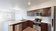 This efficient and thoughtfully designed single-floor residence offers a comfortable layout comprising a living room, kitchen, bedroom, bathroom, closet, and dedicated laundry area. The open-concept kitchen is a standout feature, equipped with stainless steel appliances including an electric range, built-in microwave, dishwasher, and refrigerator. Rich dark-brown cabinetry with sleek hardware is paired with crisp white countertops, creating a modern and functional workspace. Light wood-style flooring runs throughout the main living areas, enhancing the bright and airy atmosphere. The living room benefits from natural light streaming through multiple windows fitted with blinds, and features a ceiling fan for added comfort. The bedroom is carpeted and also includes a ceiling fan, with a window that lets in natural light. The bathroom offers a double-sink vanity with white countertops and dark cabinetry, a tub-shower combination, and wood-style flooring. A dedicated laundry area accommodates a full-sized washer and dryer set with overhead wire shelving for additional storage. A separate closet provides further organizational space. The unit's clean, neutral palette and modern fixtures create a cohesive and inviting living environment throughout.