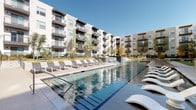 Located at 305 W Commerce St in Dallas, Texas, this outdoor amenity space is designed to deliver a resort-style experience within a modern residential community. The centerpiece is a large, beautifully maintained swimming pool with crystal-clear water, flanked on both sides by generous sun decks lined with contemporary lounge chairs and chaise lounges, ideal for relaxing under the Texas sun. A cascading water feature adds a dynamic visual element along one edge of the pool, enhancing the overall ambiance. Adjacent to the pool, a covered outdoor pavilion provides a shaded gathering area equipped with ceiling fans, mounted flat-screen televisions, and ample seating at large communal tables — perfect for outdoor dining or social events. The surrounding landscape incorporates ornamental grasses, trees, and manicured greenery that soften the hardscape and create an inviting atmosphere. A dedicated outdoor grilling station with a stainless steel built-in grill offers a convenient space for cookouts. The entire amenity area is framed by the multi-story residential building, featuring private balconies that overlook the courtyard. The space strikes a balance between active recreation and relaxed outdoor living, making it a well-appointed communal environment in the heart of Dallas.