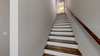This three-story residence offers a well-organized layout distributed across three levels, providing functional living spaces throughout. The ground floor serves as a compact entry level, while the main living areas occupy the more generously sized middle floor, and the upper floor accommodates additional bedrooms and bathrooms.

The combined kitchen and living room forms the heart of the home, featuring rich hardwood flooring that flows throughout much of the space. The living area is fitted with a ceiling fan and benefits from natural light through multiple windows with blinds. The kitchen is well-appointed with rich, dark-toned cabinetry, granite countertops, a white subway tile backsplash, and a full suite of stainless steel appliances including a range, microwave, dishwasher, and refrigerator.

The three bedrooms feature hardwood flooring and receive natural light through large windows. The primary bedroom includes access to a dedicated closet. The three bathrooms are finished with hexagonal tile flooring; one features a standalone glass-enclosed shower with a dark vanity, while another includes a full tub-shower combination. Two staircases with dark wood treads and white risers connect the floors, complemented by hallways that ensure smooth circulation throughout the home.