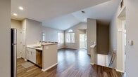 Located at 9147 W Cross Dr in Littleton, Colorado, this single-floor home offers a thoughtfully designed open layout with a variety of standout architectural features. The living area is anchored by soaring vaulted ceilings that create an expansive, airy atmosphere, complemented by a tiled fireplace with a clean white mantel and abundant natural light streaming through large windows, including a distinctive arched window accent. Rich, dark hardwood-style flooring flows throughout the main living areas, adding warmth and continuity to the space.

The kitchen is positioned as a central hub, featuring a peninsula with a built-in sink, white cabinetry, light countertops, and stainless steel appliances including a refrigerator and microwave. Recessed lighting highlights the kitchen's functional layout, which opens seamlessly into the dining and living areas — ideal for entertaining or everyday living.

The bedrooms are carpeted and bathed in natural light from large windows, with vaulted ceilings extending into these private retreats to maintain the home's sense of openness. Two bathrooms serve the residence: one featuring a full tub/shower combination, and another with a shower and a sleek white vanity with modern hardware. The neutral color palette throughout lends the home a clean, versatile aesthetic well-suited to a variety of interior styles.