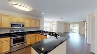 This two-story residence is designed with a functional, open layout that connects the main living areas seamlessly. The kitchen serves as a central hub on the main floor, equipped with stainless steel appliances including a refrigerator, electric range, and built-in microwave. Light wood cabinetry provides ample storage, while dark granite countertops extend across generous workspace and wrap around a peninsula that opens directly to the living and dining areas. Dark hardwood-style flooring runs throughout the main level, complementing the neutral color palette. Sliding glass doors allow natural light to fill the living space and provide access to an outdoor area.

The upper level hosts multiple bedrooms, each finished with plush wall-to-wall carpeting and windows that invite natural light and outdoor views. At least one bedroom includes a walk-in closet with built-in wire shelving, offering organized storage. Bathrooms feature light wood vanities with dark countertops, tile flooring, and a tub-shower combination with a window above. A dedicated laundry area accommodates a full-sized washer and dryer side by side, adding everyday convenience. The overall ambiance is clean, neutral, and move-in ready.