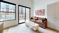 Located at 201 Grand Blvd in the heart of Kansas City, MO, this efficiently designed single-floor unit offers a thoughtfully arranged layout comprising a kitchen, living room, and full bathroom. The kitchen is a standout feature, outfitted with sleek gray cabinetry, open shelving, a white subway tile backsplash, light stone countertops, and a full suite of stainless steel appliances including a refrigerator, dishwasher, range, and microwave. Warm wood-tone flooring runs throughout, complementing the modern, neutral palette. A marble-topped dining table with a plush accent chair adds an elegant touch to the kitchen area. The living room is bright and airy, with crisp white walls, elevated ceilings with exposed structural beams, and large black-framed windows and a sliding glass door that open to a private balcony with urban views. The bathroom is clean and minimal, featuring large-format tile walls and floors, a soaking tub with shower, and a modern vanity. Throughout the unit, the design is cohesive and contemporary, maximizing every inch of the space with purposeful, stylish details that create a comfortable and functional urban living environment.