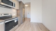 This thoughtfully designed one-bedroom, two-bathroom unit offers a clean, modern aesthetic throughout its efficiently arranged single-floor layout. Light wood laminate flooring runs seamlessly through the main living areas, complementing the crisp white walls and creating a bright, airy atmosphere.

The entrance hall welcomes you with a warm wood-toned built-in storage panel and sliding door, leading into an open-concept kitchen and living area. The contemporary kitchen is well-appointed with two-tone cabinetry in cream and wood grain finishes, a tiled backsplash, stainless steel appliances including a refrigerator, electric range, built-in microwave, and dishwasher, along with a undermount sink — providing a functional and stylish cooking space.

The bedroom is bathed in natural light through large floor-to-ceiling windows and a sliding glass door that opens to a balcony, offering open urban views. A sliding closet door adds practical storage while maintaining the room's clean lines.

The primary bathroom features neutral marble-look tile flooring, a soaking tub, a wood-grain vanity with a white countertop, and a mirrored medicine cabinet, with natural light filtering through a side window. The second bathroom provides a streamlined design with a wood-grain vanity, grab bar, and tiled flooring, offering added convenience for guests.