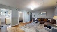 Located at 1602 18th Ave S in Nashville, TN, this two-bedroom, one-bathroom single-story home offers a thoughtfully arranged layout with a warm, cohesive aesthetic. Warm hardwood flooring runs throughout the main living areas, complemented by soft gray walls and bold dark-painted interior doors that add a contemporary contrast.

The living room is an inviting, light-filled space featuring a large window with blinds, a flush-mount ceiling light, and an open sightline into the dining room. The adjacent dining room is defined by a pendant light fixture and natural light filtering through sheer curtains, creating a relaxed atmosphere for meals.

The kitchen features stainless steel appliances, including a full-size refrigerator and range, granite-style countertops, subway tile backsplash, and modern gray cabinetry with open shelving—compact yet fully equipped.

The primary bedroom is a comfortable retreat with windows on two walls, offering natural light and a walk-in closet. The second bedroom similarly features windows and ample space. Both rooms maintain the home's consistent gray-toned palette.

The bathroom is clean and classic, with a tiled tub-shower combination, a window for ventilation, and a white finish throughout. Notably, the home offers an impressive eight closets, ensuring exceptional storage capacity across the floor plan.