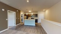 This well-designed single-floor residence offers a thoughtfully laid-out open-concept floor plan that seamlessly connects the living and kitchen areas. The kitchen is a standout feature, showcasing rich dark-toned cabinetry, crisp white quartz countertops, and a full suite of stainless steel appliances including a refrigerator, electric range, and built-in microwave. A generously sized kitchen island with an undermount sink serves as both a functional workspace and a natural gathering point, illuminated by stylish pendant lighting overhead. Wood-look flooring runs throughout the kitchen and common areas, transitioning to plush carpet in the living and bedroom spaces. The open living area is spacious and bright, with a neutral color palette accented by a warm taupe feature wall, creating a welcoming ambiance. A dedicated in-unit stacked washer and dryer adds everyday convenience. The bedroom offers comfortable carpeted flooring and a window with views of mature trees and greenery, filling the room with natural light. Sliding glass doors from the living area lead to a private balcony, further enhancing the connection to the outdoors. The bathroom is finished with a wood-toned vanity, white countertop, and wood-look tile flooring, completing this move-in ready space.