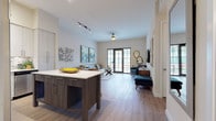 This well-appointed single-floor residence offers a thoughtfully designed open-concept layout that seamlessly connects the kitchen, dining, and living areas. The kitchen is outfitted with crisp white cabinetry, quartz countertops, stainless steel appliances, a decorative tile backsplash, and a central island that serves as both a prep space and gathering point. The living area is bright and welcoming, featuring wood-look flooring, track lighting, and glass doors that open to an outdoor space, allowing ample natural light to fill the room. A dedicated media area with a wall-mounted TV and stylish wood credenza provides a comfortable retreat within the living space. A private office accommodates dual workstations and benefits from natural light through window blinds, making it well-suited for remote work. The bedroom is a serene space with plush carpet, dual windows fitted with layered blinds, and direct access to a generously sized walk-in closet with built-in shelving and hanging rods. A clean, light-filled half bath features white cabinetry and wood-look flooring. Completing the unit is a dedicated laundry room with a full-size top-loading washer and dryer. Throughout, neutral tones and modern finishes create a cohesive and functional living environment.
