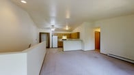 This single-floor unit offers a practical and comfortable layout centered around an open-concept living and kitchen area. The living space features soft carpeting and a ceiling fan overhead, creating a relaxed and functional atmosphere. The kitchen is equipped with warm wood-toned cabinetry, a white refrigerator, a range, and a peninsula counter that defines the space while maintaining an open flow to the living area. Durable tile-style flooring runs through the kitchen, complementing the neutral tones throughout.

A walk-in closet provides generous storage, while additional doorways lead to other areas of the unit, suggesting a well-organized floor plan. The interior is finished with clean white walls and simple, classic trim details that contribute to a bright and neutral aesthetic.

One of the standout features of this space is the private outdoor deck, which overlooks a lush canopy of mature trees. The deck is framed by warm wooden railings and offers a peaceful, nature-filled retreat with open sky above. This outdoor space adds a natural ambiance that complements the overall character of the unit, making it an inviting place to relax while enjoying the surrounding greenery.