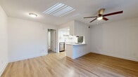 Located in Austin's sought-after 78704 zip code, this two-bedroom, one-bathroom unit offers a practical and well-designed single-floor layout. The combined kitchen and living area forms the heart of the home, anchored by light wood-look flooring that runs throughout. The kitchen features white cabinetry with subway tile backsplash, stainless steel appliances including a dishwasher and refrigerator, a built-in cooktop on the peninsula, and a white countertop breakfast bar — ideal for casual dining or meal prep. A skylight panel above the kitchen floods the space with natural light, while a ceiling fan in the living area promotes comfortable airflow. Vertical blinds cover a sliding glass door that opens to an outdoor area, bringing additional natural light into the living space. The two bedrooms are carpeted and each equipped with a ceiling fan, offering a cozy and quiet retreat. One bedroom features a window with blinds that allows natural light to filter in. The bathroom is clean and functional, appointed with large-format white subway tile surrounding a full soaking tub and shower combination with brushed gold fixtures. A dedicated closet provides additional storage. The overall aesthetic is clean, bright, and move-in ready.