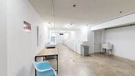 Located at 300 Francis Street in Branson, Missouri, this commercial laundry facility offers a generously sized, single-floor layout designed for efficient, high-capacity laundering operations. The space is defined by its clean, all-white walls and polished concrete floors, creating a bright and utilitarian environment that is easy to maintain.

The main laundry area is the centerpiece of the facility, featuring two long rows of commercial-grade washers and dryers lining opposite walls, providing ample machine capacity for heavy usage. Fluorescent lighting runs along the ceiling, ensuring the entire space is well-illuminated throughout the day. A utility sink is also present, adding functional convenience.

Adjacent to the laundry area is a large open secondary space, characterized by exposed overhead piping and conduit running along the ceiling, giving it an industrial character. This area includes a wooden-topped work table with a sleek black metal frame and a light blue molded chair, offering a waiting or folding area for users. A bulletin board and framed laundry-themed artwork add a touch of personality to the otherwise minimal décor.

The facility also features a climate control unit mounted to the ceiling, ensuring comfort year-round. Multiple doorways connect the sections of the space, and the overall layout flows in a practical, linear fashion. The facility is well-suited for serving a multi-unit residential building or similar high-demand setting.