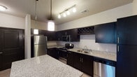 This single-floor residence in Wyoming, Michigan offers a well-designed layout with contemporary finishes throughout. The kitchen serves as a standout feature, outfitted with dark espresso cabinetry, light granite countertops, and a full suite of stainless steel appliances including a refrigerator, range, over-the-range microwave, and dishwasher. A built-in wine rack adds a distinctive touch, while pendant and track lighting illuminate the space effectively. A large granite-topped island provides additional prep and seating space. The kitchen flows into an open living area finished with smooth, light-toned wood-look flooring, neutral walls, and a ceiling fan that enhances comfort and airflow. Natural light enters through a window, adding brightness to the generous living space. The bedroom features plush carpeting, a ceiling fan, and multiple windows that invite natural light and outdoor views. Dark-toned interior doors provide a consistent design accent throughout the unit. The bathroom is clean and functional, featuring a full tub-shower combination with a curved rod, light wood-look flooring, and granite-accented vanity. A utility panel is conveniently accessible within the unit. Overall, the space presents a cohesive modern aesthetic with practical, quality finishes.