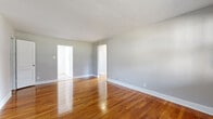 This single-floor unit offers a cohesive and functional layout characterized by warm, polished hardwood flooring that runs throughout most of the living spaces, complemented by neutral gray walls and crisp white trim. The open living and dining areas are connected through arched doorways, creating an inviting flow between rooms. Multiple bedrooms are generously proportioned, each featuring large windows with blinds that allow abundant natural light to fill the space; several rooms are equipped with radiator heating units, and one room includes a wall-mounted air conditioning unit. One bedroom features a ceiling fan, adding to the comfort of the space. A smaller room with light wood-look tile flooring provides flexible use as a home office or additional living area. The kitchen is well-equipped with rich mahogany-toned cabinetry, a light gray subway tile backsplash, white countertops, and a full suite of stainless steel appliances including a range, microwave, dishwasher, and refrigerator. The bathroom is finished with classic white subway tile walls accented by a gray border strip, a soaking tub, a vanity with sink, and a window that provides natural ventilation. Throughout, the space maintains a clean, move-in-ready presentation.