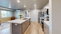 Located at 925 E Omaha St in Rapid City, South Dakota, this 2-bedroom, 1-bathroom unit offers a thoughtfully designed layout across a single floor. Light-toned luxury vinyl plank flooring runs throughout, complementing the neutral gray walls and clean white trim that give the space a modern, cohesive feel.

The kitchen serves as a functional centerpiece, featuring gray flat-front cabinetry, white countertops, a central island with a built-in sink, and a full suite of stainless steel appliances including a refrigerator, range, microwave, and dishwasher. Recessed lighting illuminates the space efficiently.

Both bedrooms offer a calm, minimalist atmosphere with ample wall space and natural light. The primary bedroom includes a sliding closet, while the second bedroom benefits from a large window with outdoor views. The full bathroom is clean and practical, with LVP flooring, a shower with curtain, and a vanity with gray cabinetry.

A dedicated laundry room houses a full-size washer and dryer with overhead wire shelving for added storage. A connecting hallway ties all rooms together in a logical, accessible flow, making this a practical and comfortable residential space.