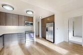 Located at 1115 SW Market St in Portland, Oregon, this well-appointed 2-bedroom, 3-bathroom residence offers a thoughtfully designed single-level layout. The open living room is bathed in natural light, courtesy of expansive floor-to-ceiling sliding glass doors that lead to a private balcony overlooking lush, tree-lined surroundings — a standout feature of the space.

The kitchen is efficiently designed with warm walnut-toned cabinetry extending to the ceiling for ample storage, light quartz countertops, a herringbone tile backsplash, and a full suite of stainless steel appliances including a French door refrigerator, electric range, over-the-range microwave, and dishwasher. Light wood-style flooring flows throughout the main living areas, complementing the clean, modern aesthetic.

The primary bedroom is a comfortable retreat featuring plush carpet, corner windows that invite natural light and outdoor views, and a dedicated en-suite bathroom with a stone-topped vanity, warm wood cabinetry, and a large mirror. The second bedroom also features soft carpeting and connects to its own bathroom. All three bathrooms echo a consistent modern design with quartz countertops and wood-toned vanities. The space is finished with crisp white walls and flush-mount lighting throughout.