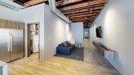 Located at 1011 W 1st St in downtown Spokane, this three-bedroom, two-bathroom loft masterfully combines industrial heritage with contemporary design. The exposed wood beam ceilings, visible ductwork, and original brick accent walls create a striking backdrop throughout, while light hardwood flooring and a neutral palette keep the aesthetic clean and modern.

The kitchen is a standout feature, showcasing a large center island with seating, sleek wood-grain cabinetry, quartz countertops, a mosaic tile backsplash, and stainless steel appliances. Natural light pours in through a large original-frame window framed by exposed brick, adding warmth and character. The living area flows naturally from the kitchen, featuring track and pendant lighting beneath the dramatic open-beam ceiling.

The primary bedroom offers a serene retreat with an exposed brick accent wall providing rich texture and ambiance. The bathrooms are finished with large-format stone tile, including a walk-in glass-enclosed shower with mosaic tile flooring. A dedicated in-unit laundry room adds everyday convenience. The tiled entryway offers a clean and welcoming transition into the space. Throughout, the design strikes a refined balance between historic industrial charm and thoughtful modern living.