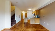 Located at 401 N Carroll St in Madison, Wisconsin, this two-floor unit offers a practical and well-organized layout across both levels. The main floor features an open-concept living and kitchen area with warm hardwood-style flooring throughout. The kitchen is equipped with oak cabinetry, granite-style countertops, a peninsula with pendant lighting, and white appliances including a refrigerator and range. A staircase with carpeted treads connects the main level to the upper floor, with an adjoining half bathroom on the main level featuring tile flooring and a pedestal sink. The open living area provides generous space, clean white walls, and a straightforward, functional design. Upstairs, the bedrooms are carpeted and feature corner and standard windows that allow natural light and treetop views of the surrounding greenery. Baseboard heating and individual wall air conditioning units are present in the upper-level rooms. A full bathroom on the upper level includes an oak vanity with a wide mirror and a shower-tub combination. The overall aesthetic is clean and functional, with a neutral color palette, durable flooring choices, and ample natural light throughout both floors.