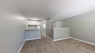 Located at 6300 N Broadway St in Kansas City, Missouri, this single-floor, one-bedroom, one-bathroom unit offers a practical and well-organized layout. The open living area greets you upon entry, featuring neutral-toned carpet, gray walls with crisp white baseboards, and a textured ceiling that adds visual interest overhead. A half-wall partition separates the living space from the kitchen, which is equipped with white cabinetry, a refrigerator, and a granite-style countertop that extends to form a functional breakfast bar. The layout flows naturally from the living area through a corridor leading to the private spaces. The spacious bedroom offers generous square footage, plush carpeting, and a window that brings in natural light, creating a comfortable retreat. A dedicated closet provides convenient storage. The bathroom is finished with wood-look tile flooring, a white vanity with a granite-style countertop, a toilet, and a full-size soaking tub with a white surround. Throughout the unit, the consistent gray color palette, white trim, and clean finishes give the space a cohesive, move-in-ready aesthetic suited for practical everyday living.
