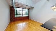 Located at 237 Jacksonville Rd in Hatboro, PA, this two-floor loft seamlessly blends industrial character with modern finishes. The space is defined by its striking exposed brick walls, soaring ceilings with open structural trusses, and visible ductwork that lend an authentic industrial aesthetic throughout. Hardwood flooring flows through the main living areas, complemented by plush carpet in the secondary rooms, providing a warm contrast to the raw architectural elements.

The kitchen is a standout feature, showcasing warm wood cabinetry, dark granite countertops, stainless steel appliances including a gas range and refrigerator, and bold pendant lighting suspended from the dramatic ceiling. A breakfast bar adds functional counter space and an open connection to the living area.

Carpeted rooms with exposed brick accent walls offer versatile spaces, each bathed in natural light from large windows with views of the surrounding area. The bathroom is finished with clean white subway tile, dark granite vanity surfaces, rich wood cabinetry, and slate-toned floor tiles, creating a crisp, contemporary feel. A stacked washer and dryer unit is conveniently integrated into the bathroom area. The overall ambiance is one of urban sophistication, balancing historic industrial character with thoughtful modern updates.