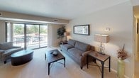 This single-floor residence offers a thoughtfully designed open layout that seamlessly connects its primary living areas. The living room is bright and welcoming, anchored by large sliding glass doors that open to a private balcony overlooking lush outdoor greenery, allowing abundant natural light to fill the space. Soft carpeting and neutral tones throughout create a warm, cohesive ambiance.

The kitchen is well-equipped and functional, featuring warm wood cabinetry, granite countertops, a stainless steel sink, and black appliances including a gas range, dishwasher, and full-size refrigerator. A peninsula counter provides additional workspace and a natural transition into the dining area, which is highlighted by an elegant pendant light fixture overhead.

The primary bedroom is generously proportioned with plush carpet, a large window framing views of the surrounding landscape, and ample space for furnishings. A second bedroom offers similar comfort with natural light and outdoor views. A flexible bonus room serves well as a home office or sitting area.

The bathrooms are finished with tasteful detail. The primary bath features a stepped marble-surround soaking tub with grab bars, while the secondary bath includes a granite-topped vanity with white cabinetry, marble-style tile flooring, and a walk-in shower. The overall design balances practicality with comfort throughout.
