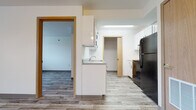 This single-floor unit offers a clean, modern aesthetic with wood-look plank flooring carried consistently throughout the space, creating a cohesive and easy-to-maintain environment. The kitchen is efficiently designed, featuring white cabinetry with black hardware, granite-style countertops, a built-in sink, a black range, and a black refrigerator. A skylight overhead adds a touch of natural brightness to the cooking area, while an adjacent pantry or utility closet provides additional storage. The kitchen connects openly to the living area, which is generously proportioned, bright, and features a window that allows natural light to fill the room.

The bedrooms are well-sized and offer a neutral palette of white walls and wood-look flooring. Each room features windows with blinds for light control and privacy. At least one bedroom includes a sliding-door built-in closet, offering practical storage. A hallway with warm wood-toned doors connects the rooms throughout the unit.

The bathroom is thoughtfully appointed with a vanity featuring a single basin sink, granite-style countertop, and white cabinetry. Accessibility is prioritized with grab bars installed near the toilet and bathtub. The overall ambiance of the unit is clean, neutral, and move-in ready.