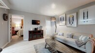 This thoughtfully designed single-floor residence combines contemporary style with practical functionality across its well-organized layout. The open-concept living area serves as the heart of the home, featuring light hardwood-style flooring, soft gray walls, and a textured ceiling that adds subtle dimension. Large windows fitted with white plantation shutters allow natural light to fill the space, creating a bright and welcoming ambiance. The living room comfortably accommodates multiple seating areas and is accented with eclectic décor, including decorative wall mirrors and curated artwork.

The kitchen flows seamlessly from the living space and is outfitted with gray shaker-style cabinetry, stainless steel appliances including a refrigerator, microwave, and range, and crisp white countertops. A peninsula with bar seating provides a convenient transition between the kitchen and living area. A stacked washer and dryer unit is conveniently integrated into the kitchen space.

The bedroom is a serene retreat, featuring the same light flooring, generous natural light from a shuttered window, and ample space for a full furniture arrangement. A vibrant piece of wall art adds a bold focal point to the room.

The bathroom is finished with large-format gray tile surrounds in the tub and shower area, offering a clean and modern aesthetic throughout.
